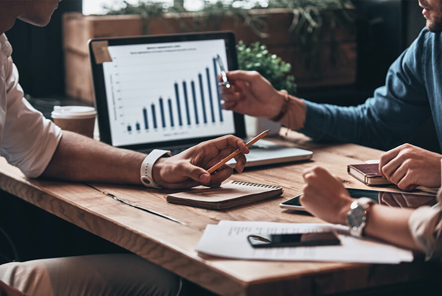 Two marketing professionals reviewing a bar chart on a laptop during a strategy meeting, discussing partnership marketing trends and performance data.
